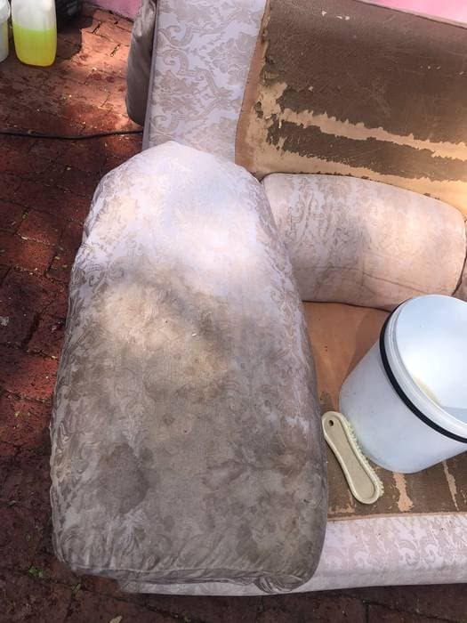 Heavily soiled armchair cushion before cleaning, with cleaning products beside it.
